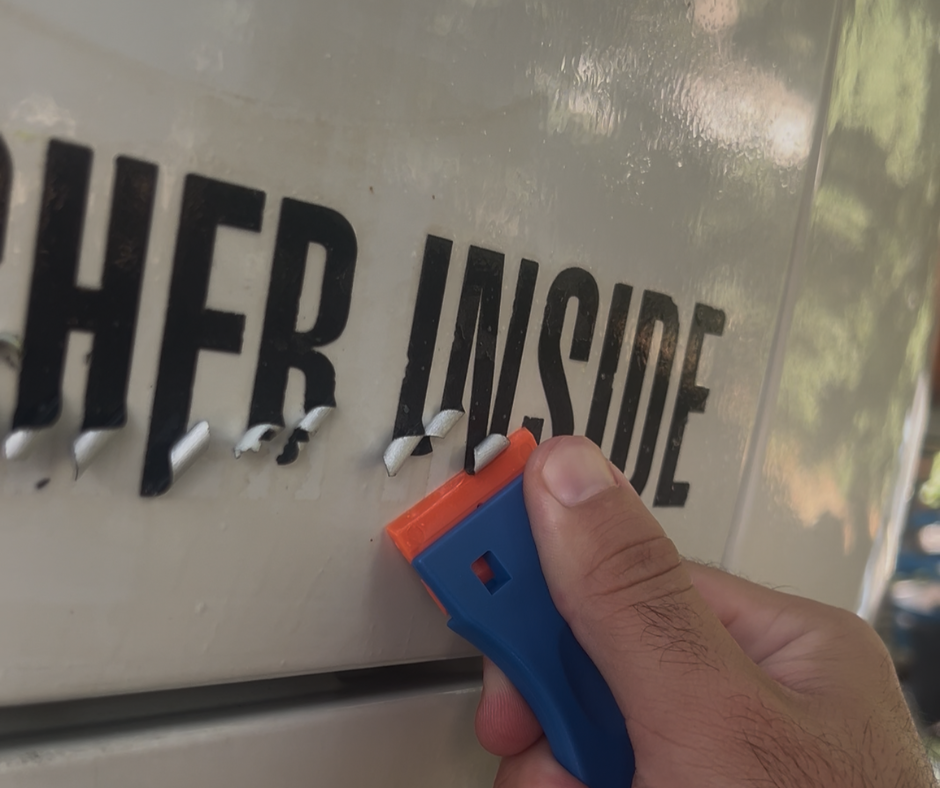 Close-up of old vinyl lettering being removed from a commercial vehicle before replacement graphics are installed.